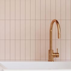 a gold faucet sitting on top of a white sink next to a pink tiled wall