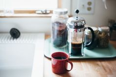 a red coffee mug sitting on top of a wooden table next to a stovetop