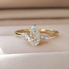 a yellow gold engagement ring with three pear shaped diamonds on the band and an oval diamond in the center