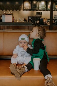 two toddlers sitting on a bench in front of a coffee shop counter with cups