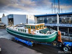 a green and white boat sitting on top of a trailer in front of a building