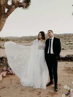 a man and woman standing next to each other in front of a joshua tree at their wedding