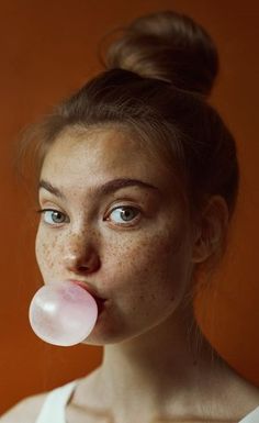 a woman with freckles on her nose blowing bubbles