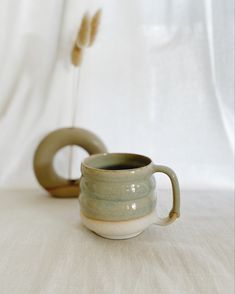 two green cups sitting on top of a table next to a white vase with an oat sticking out of it