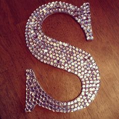 the letter s is made up of silver and crystal stones on a wooden table top