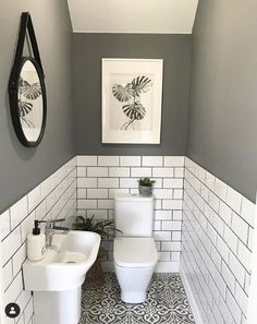 a white toilet sitting next to a sink in a bathroom under a framed plant on the wall