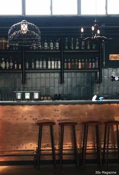 three stools at the bar with bottles on the shelves behind them and a birdcage hanging from the ceiling