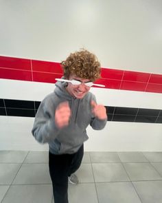 a young boy in grey sweatshirt and black pants standing on tiled floor next to wall