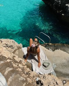 a woman sitting on top of a rock next to the ocean