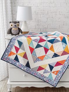 a bed with a colorful quilt on it and a teddy bear sitting next to it