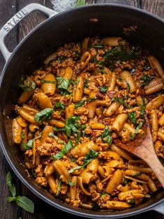 pasta with meat and spinach in a skillet on a wooden table, ready to be eaten