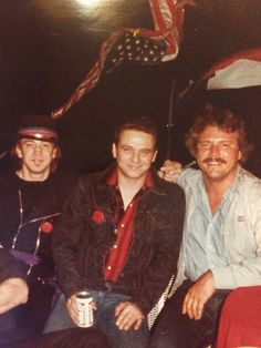 three men sitting next to each other with an american flag on the wall behind them