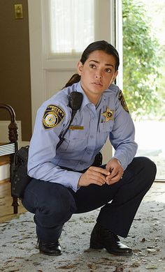 a woman police officer kneeling down in front of a door and looking at the camera