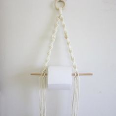 a white toilet paper holder hanging from a wall with rope and beads on the handle