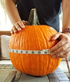 a person measuring the width of a pumpkin with a tape measure on it's side