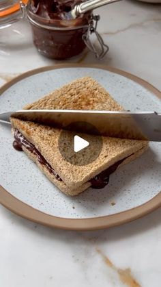 a sandwich cut in half on a plate with a knife and chocolate spread next to it