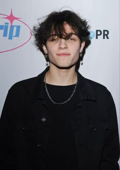 a young man with black hair and piercings standing in front of a white wall