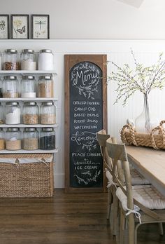 a chalkboard sign in the corner of a kitchen with jars and baskets on it