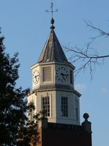 a tall clock tower with a weather vein on it's side and trees in the foreground