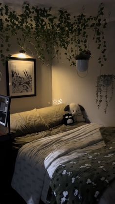 an unmade bed with plants hanging from the ceiling and a stuffed animal on it