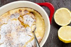 a red and white bowl filled with lemon custard cake next to sliced lemons