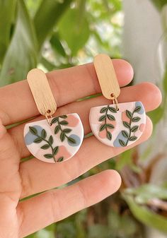 a pair of earrings with leaves painted on them in front of a green leafy background