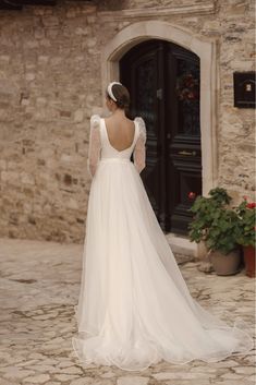 a woman in a white wedding dress standing on a cobblestone street with her back to the camera