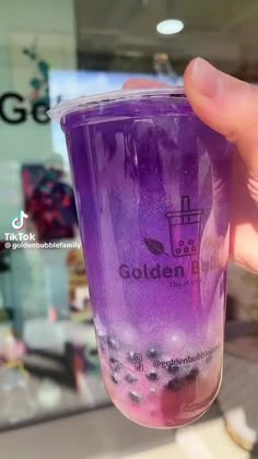 a person holding up a purple cup in front of a store window with blueberries on it