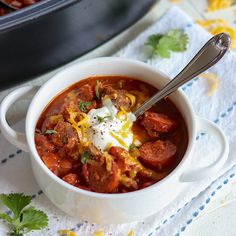 a close up of a bowl of chili with meat and sour cream on the top