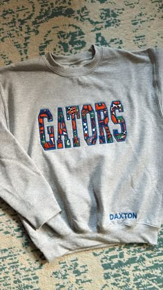 This listing is for one applique sweatshirt! 👉 To make a purchase, follow these steps: 1. Choose the color of the sweater with either GATORS or CHOMP CHOMP.  2. Select the appropriate size 4. Add the item to your cart 5. Repeat the process for any additional sweaters you'd like to purchase 6. Finalize your order Also! As seen in the first photo, there is the option to add an additional customization of your name at the bottom of the sweatshirt!  All you have to do is leave the name youd like on Iowa State Outfit, Vintage Golf Sweatshirt, College Sweatshirt Design, Diy College Apparel, Sewing Sweaters, Crewneck Design Ideas, Cute Sweatshirt Designs, Appliqué Sweatshirt, Florida Sweatshirt