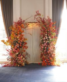 an archway decorated with flowers and greenery in front of a window at the end of a blue carpeted floor