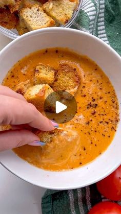 a person dipping some bread into a bowl of soup with tomatoes and other food on the side