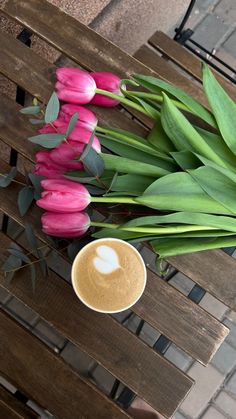 some pink tulips and a cup of coffee on a wooden table with green leaves