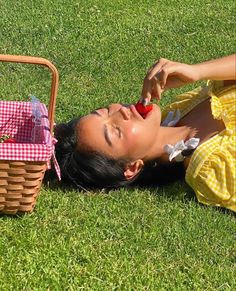 a woman laying on the grass next to a picnic basket with an apple in it