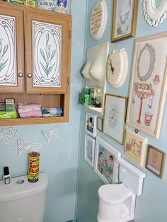 a bathroom with blue walls and pictures on the wall next to a white toilet in front of a wooden cabinet