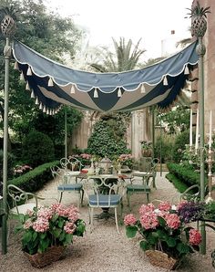 an outdoor dining area with potted plants and flowers on the table under a blue awning