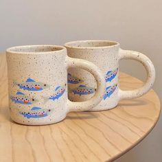 two coffee mugs sitting on top of a wooden table with fish painted on them