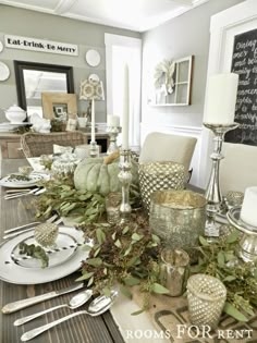 a dining room table is set with silverware and greenery for the centerpiece