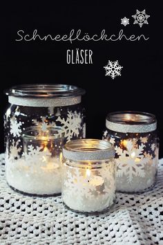 three glass jars with snowflakes on them sitting on a doily covered table