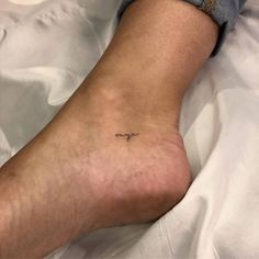 a person with a small tattoo on their foot laying in bed next to a pillow