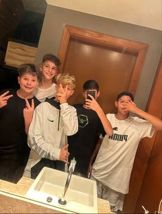 a group of young men standing in front of a bathroom mirror taking a selfie