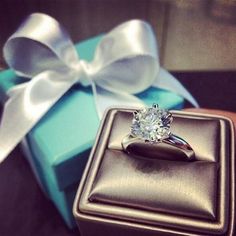 a diamond ring sitting on top of a box next to a white ribbon and bow