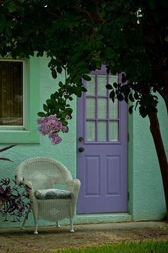 a white wicker chair sitting in front of a purple door on a green house