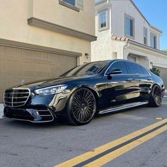 a black mercedes s - class parked in front of a house with garage doors open