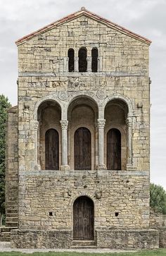 an old stone building with arched windows and two doors on the front, surrounded by green grass