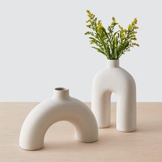 two white vases sitting on top of a table next to each other with flowers in them