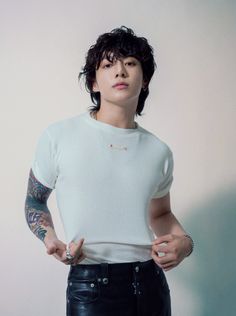 a man with tattoos standing in front of a white wall holding his hands on his hips