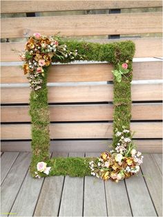 a moss covered letter with flowers and leaves on it sitting in front of a wooden wall