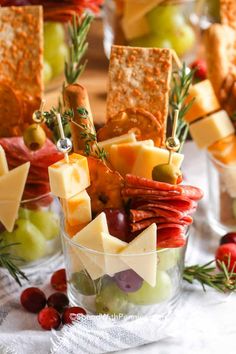 cheese, crackers and grapes are arranged in small glass bowls on a table with other snacks