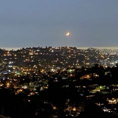 the city lights shine brightly in the night sky as seen from atop a hill with trees